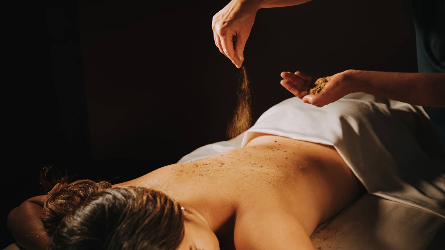 Spa staff sprinkled coffee powder over woman's bare back as she lays on massage table