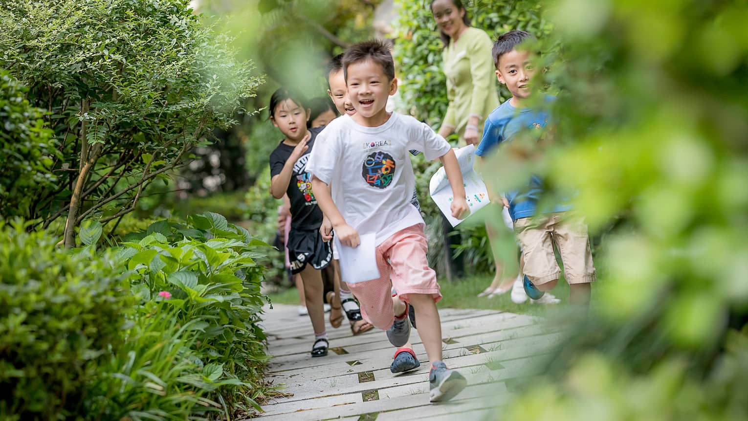Smiling children run down wood path, bridge