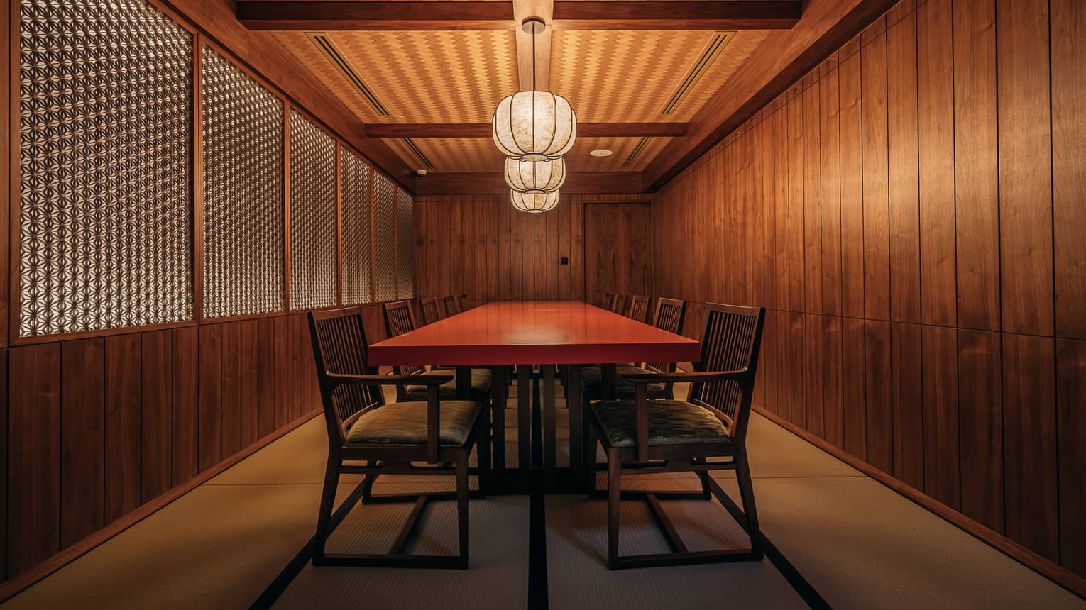 Private dining room with Japanese-style wood panelled walls and a red rectangular table in the centre sert beneath three paper lanterns