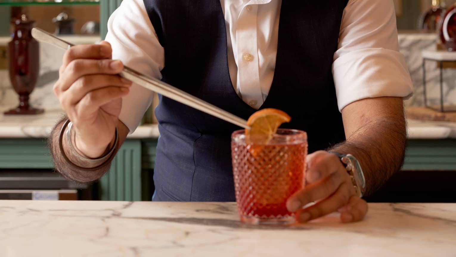 Bartender behind bar garnishing a negroni with an orange slice using long tongs
