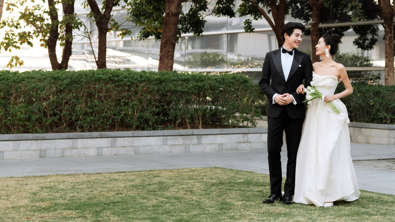 Bride and groom stand on outdoor terrace flanked by trees