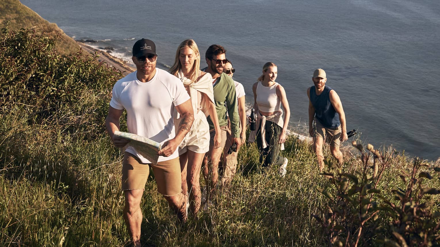 Six guests walking up a mountain with the clouds and sky in the background.