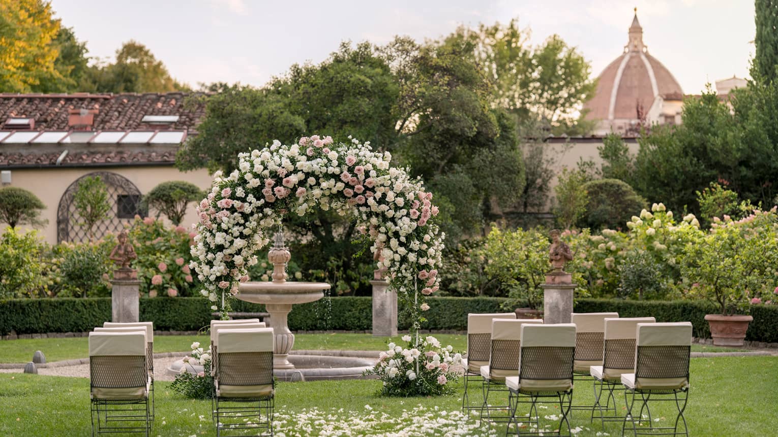 Garden wedding setup with floral archway and view of Duomo in backdrop