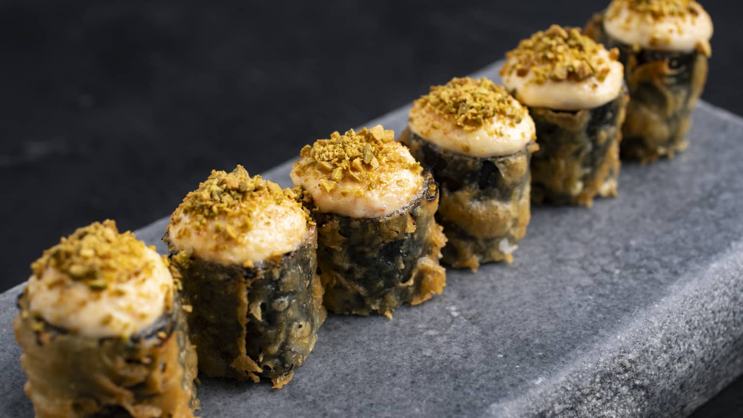 Six crispy rolls lined up in a row on a rectangular slate-grey platter