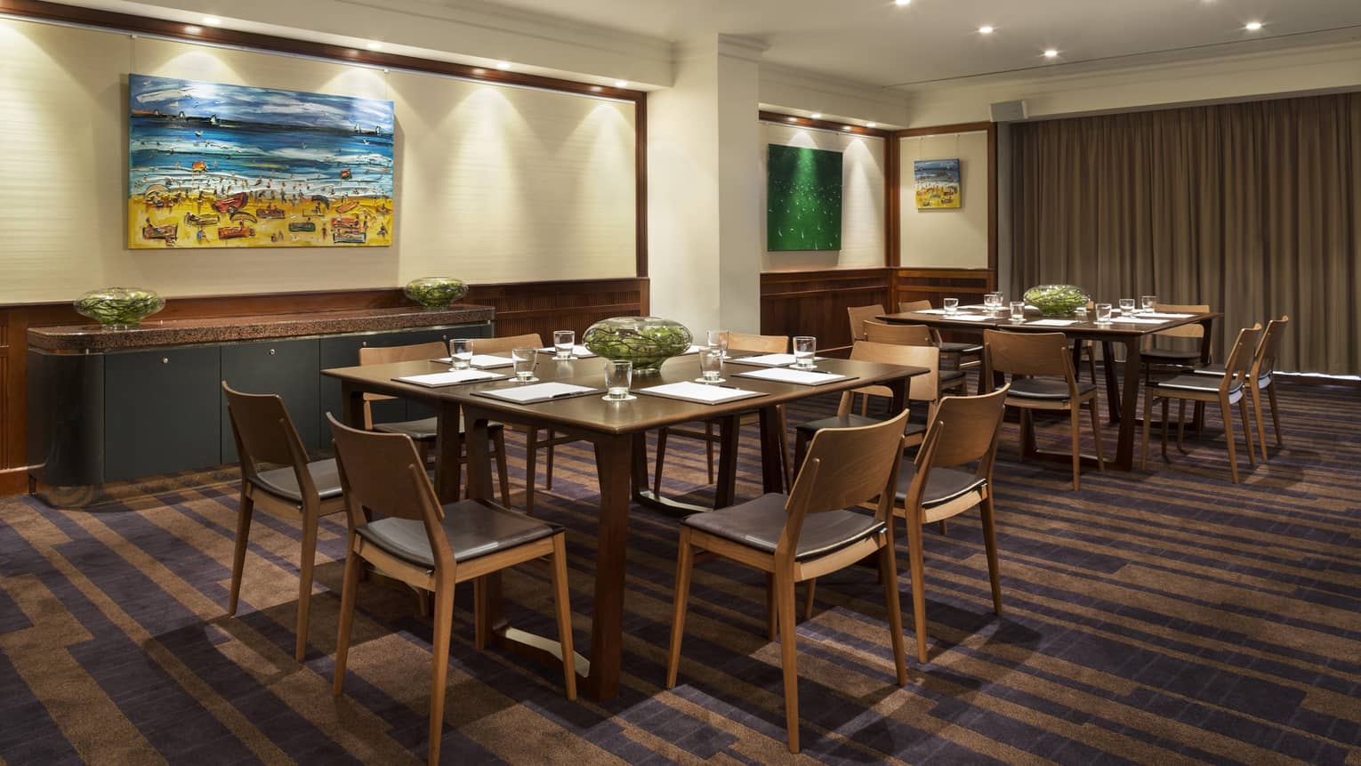 Gallery meeting room with small square tables with retro-style chairs, colourful paintings on walls