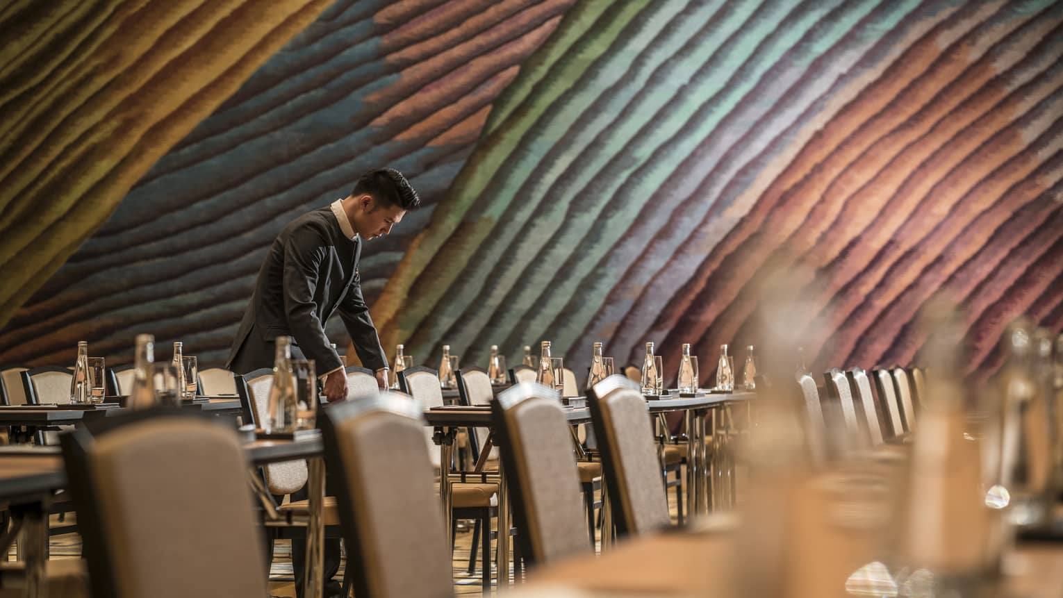 Hotel staff sets long conference meeting tables under colourful accent wall