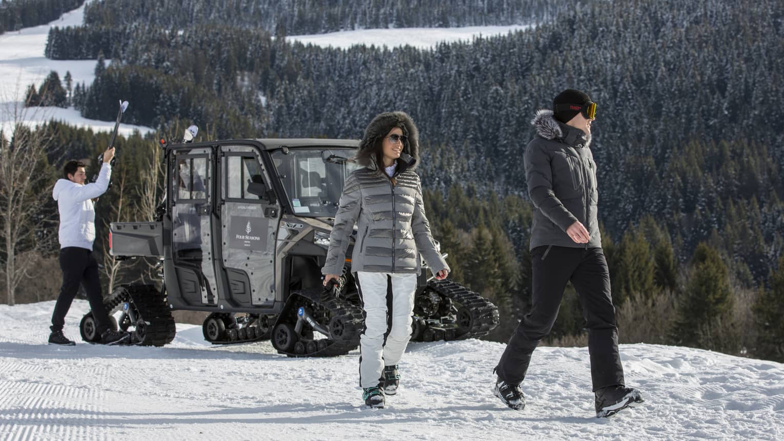 Couple walks away from ski valet large snowmobile on top of snowy mountain