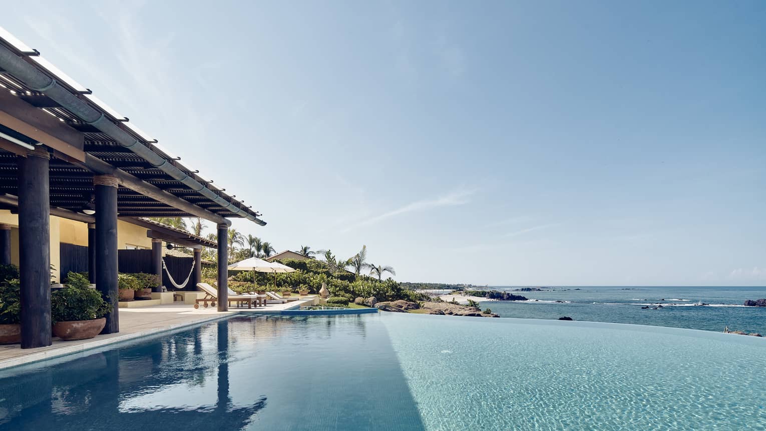 View over infinity swimming pool looking over ocean, covered patio at side
