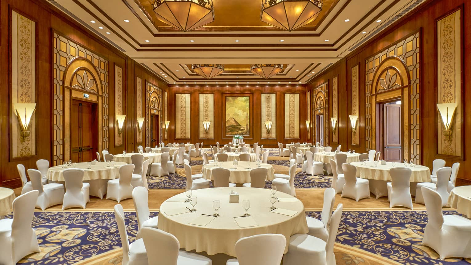 Tiran Ballroom with large white banquet tables, chairs under gold and wood Art Deco style lights, walls