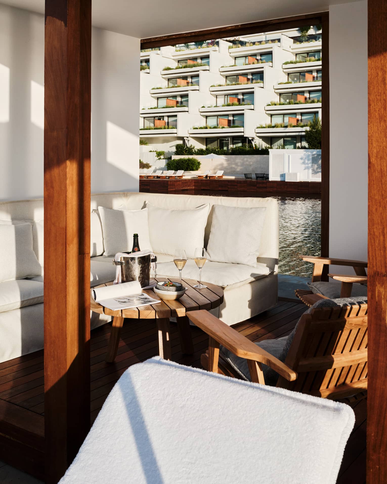 Cabana interior with white banquette-style couch, round teak table and teak chairs