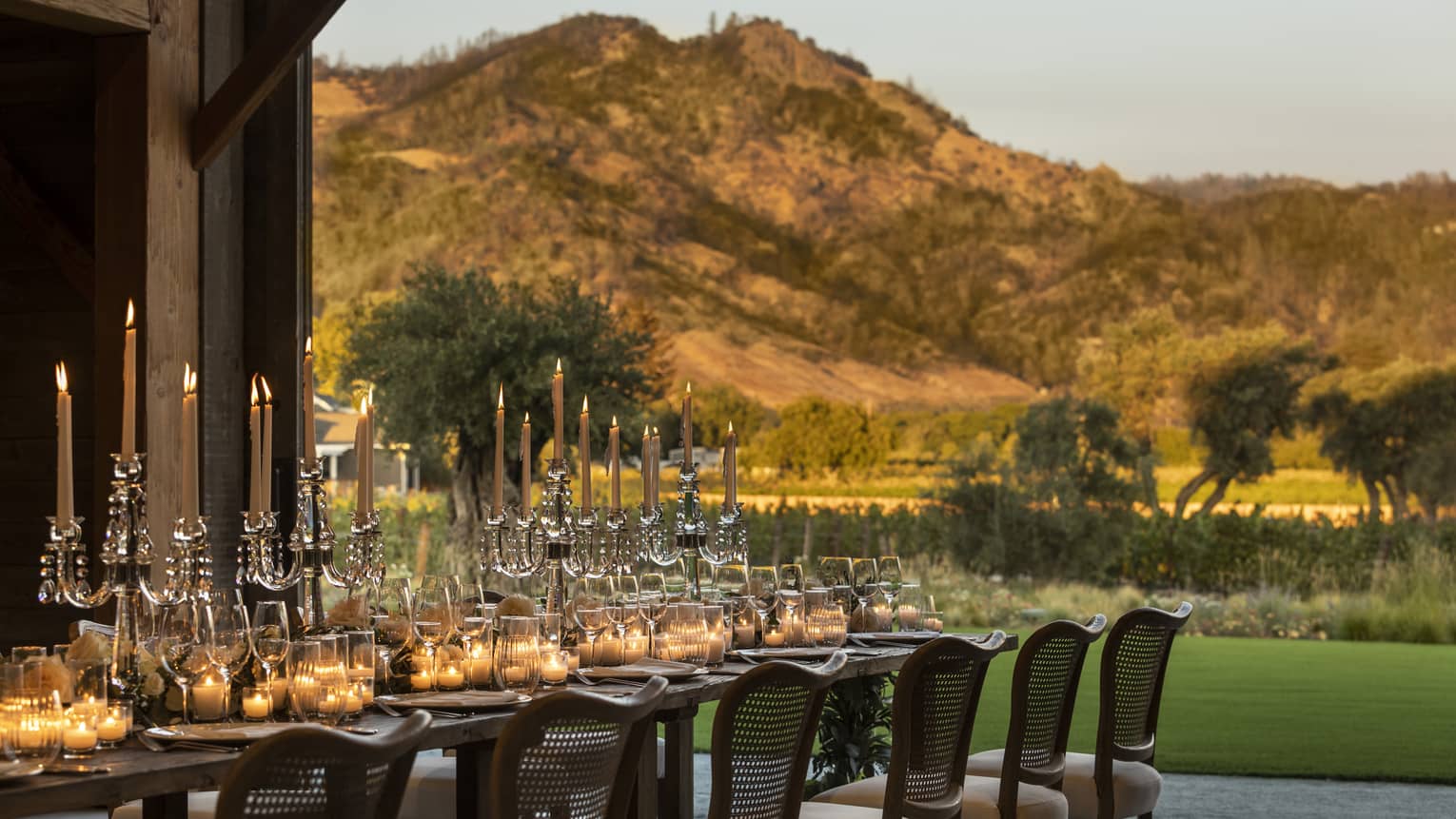 A long table with candles outside near mountains.