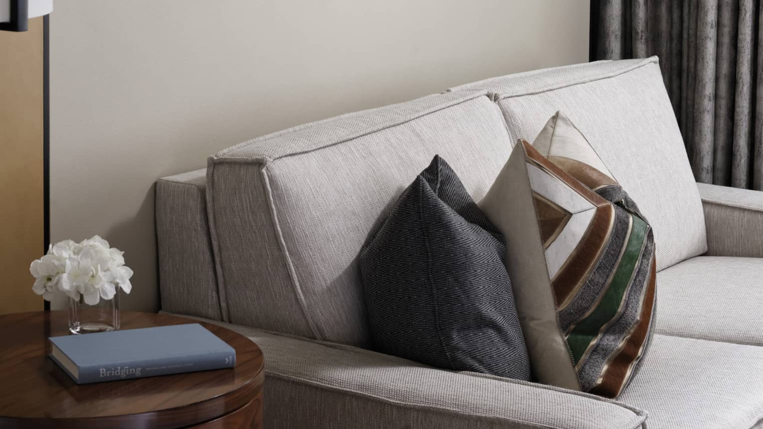 Cream loveseat, patterned accent pillows, wooden side table, wall art trio, grey curtains