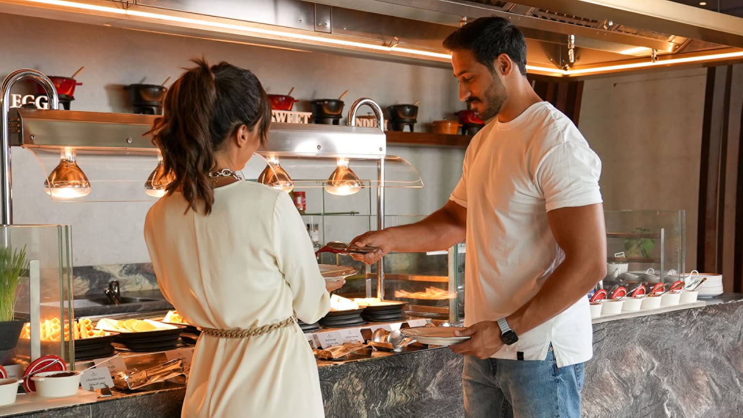 A man and woman stand serving their plates from a buffet station
