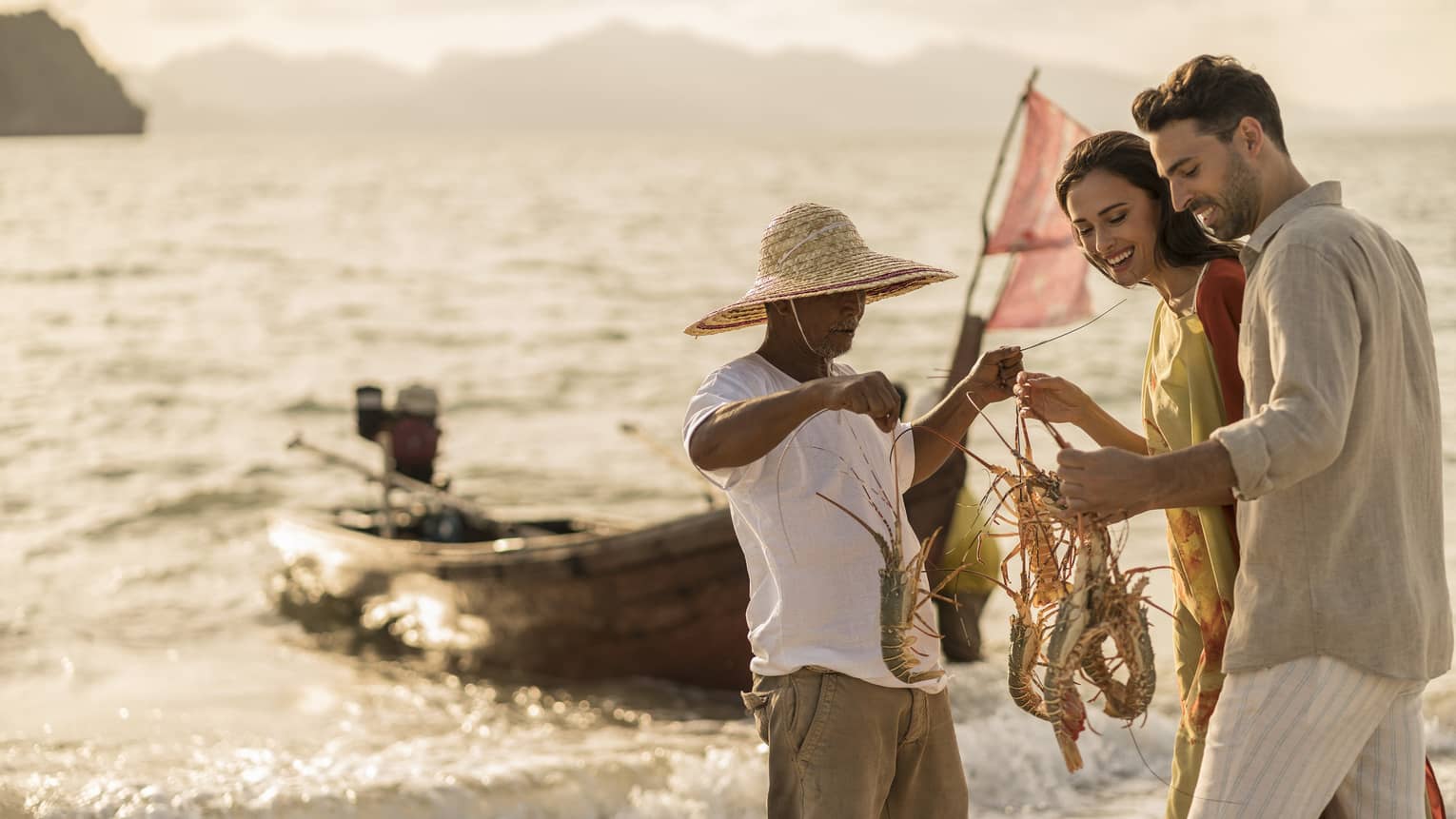 A four seaons fishing guide is holding and showing 4 lobsters to a man and a woman