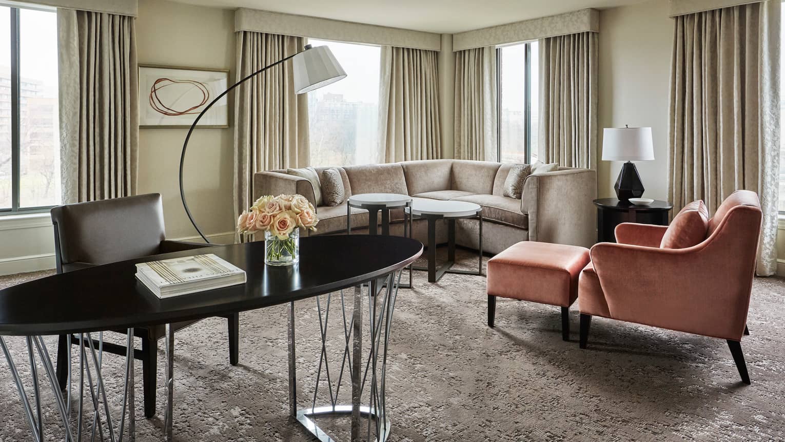 Capital Suite living room with long oval work desk in front of L-shaped sofa, pink armchair, corner windows