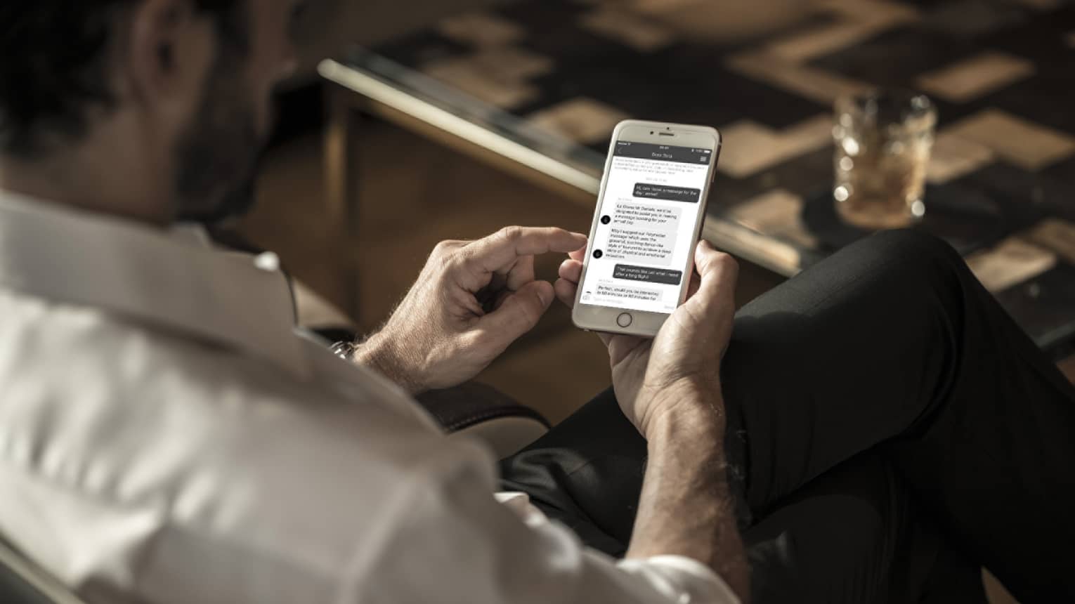 Man wearing suit looks down at text messages from spa on smart phone in lounge