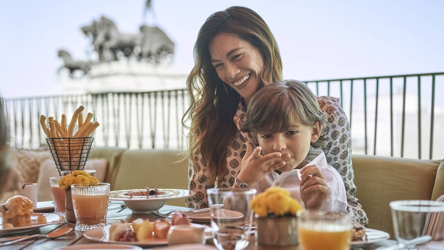 Woman and young boy sit at outdoor restaurant table with food