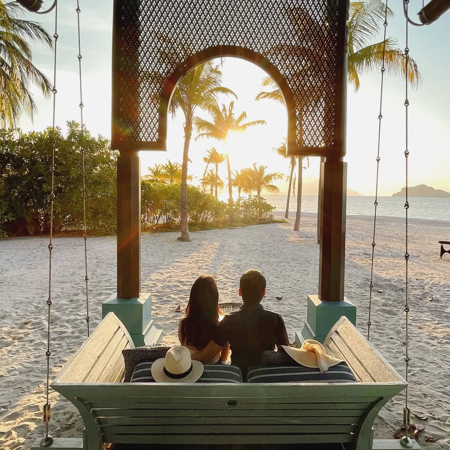 ,A couple watches the sunset from a hanging swing on the beach