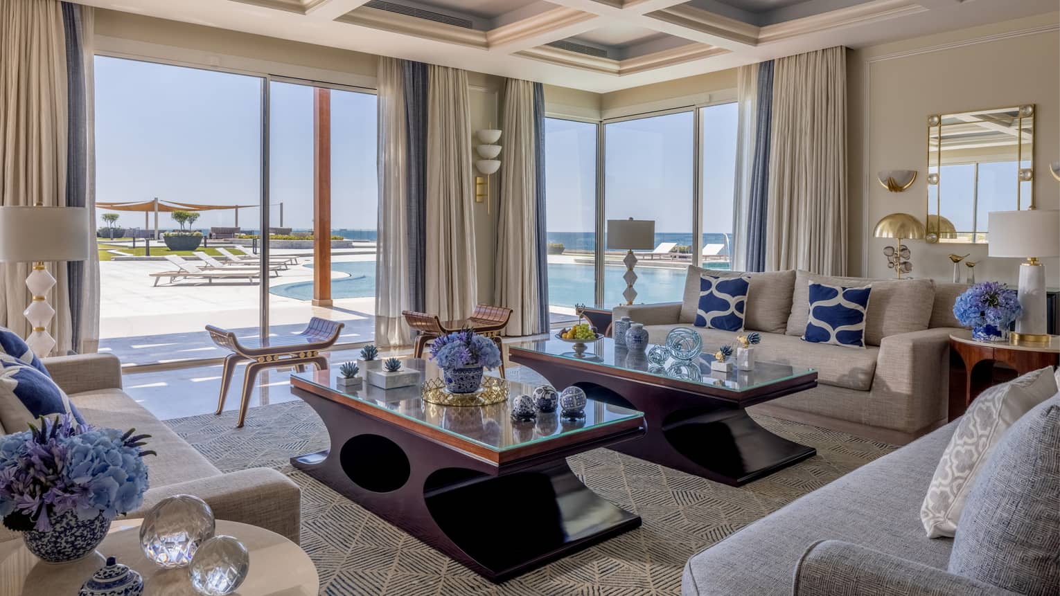 The Palace living area with cream and tan sofas, ergonomic cherry wood coffee tables, sliding glass doors to patio with pool