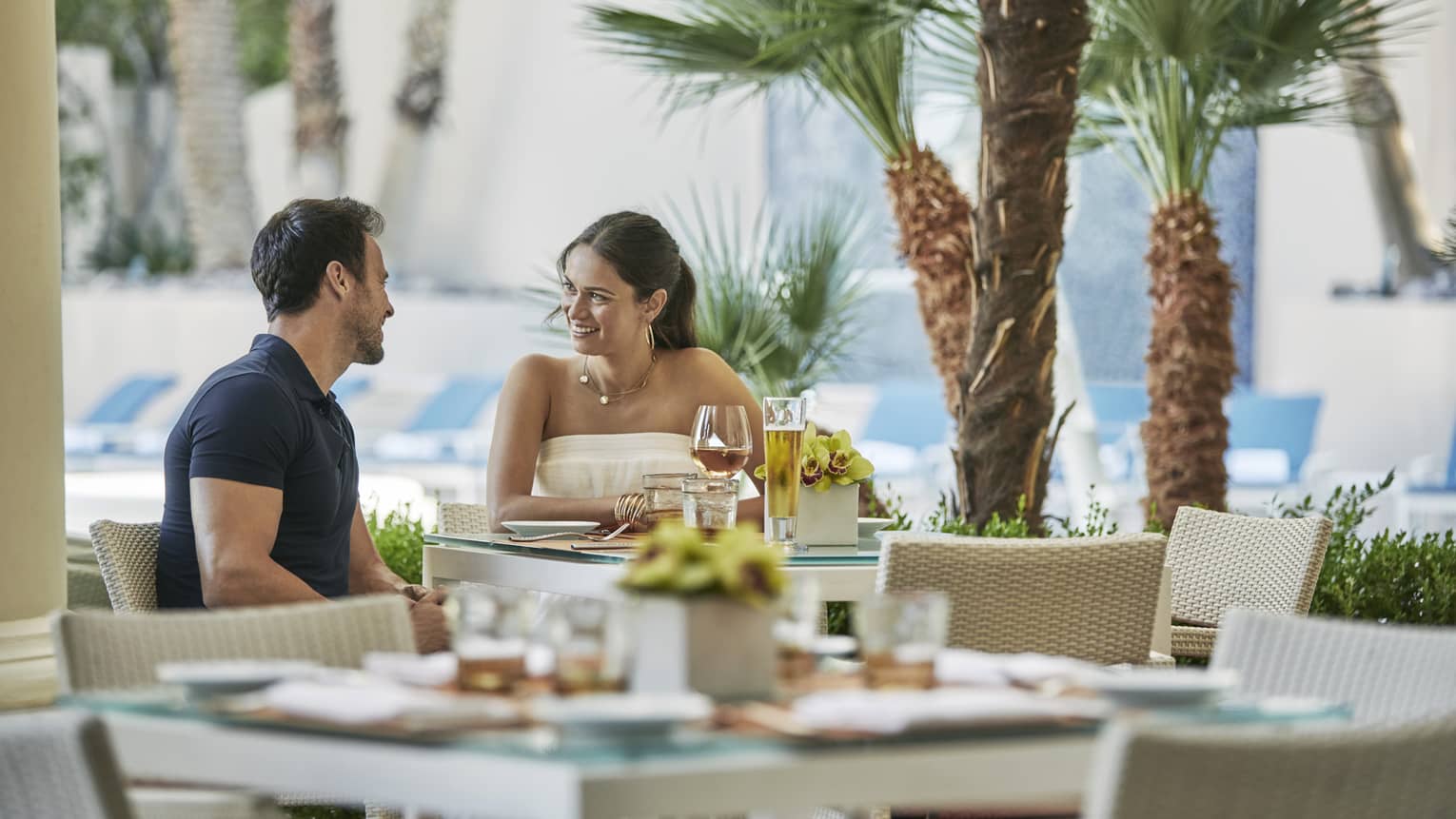 Veranda, couple dines at outdoor dining table by small palm trees 