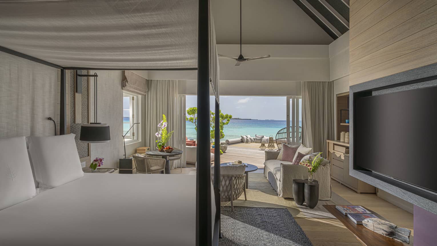 Luxury bedroom with four-poster bed, sitting area and walk-out terrace facing tropical beach