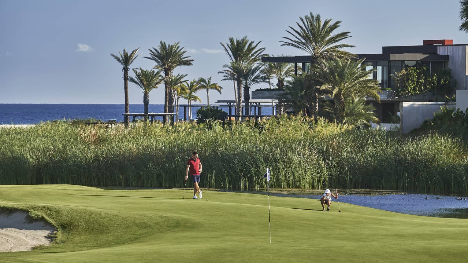 Two golfers enjoy a day on the golf course at four seasons Los Cabos with palm trees and the ocean in the background
