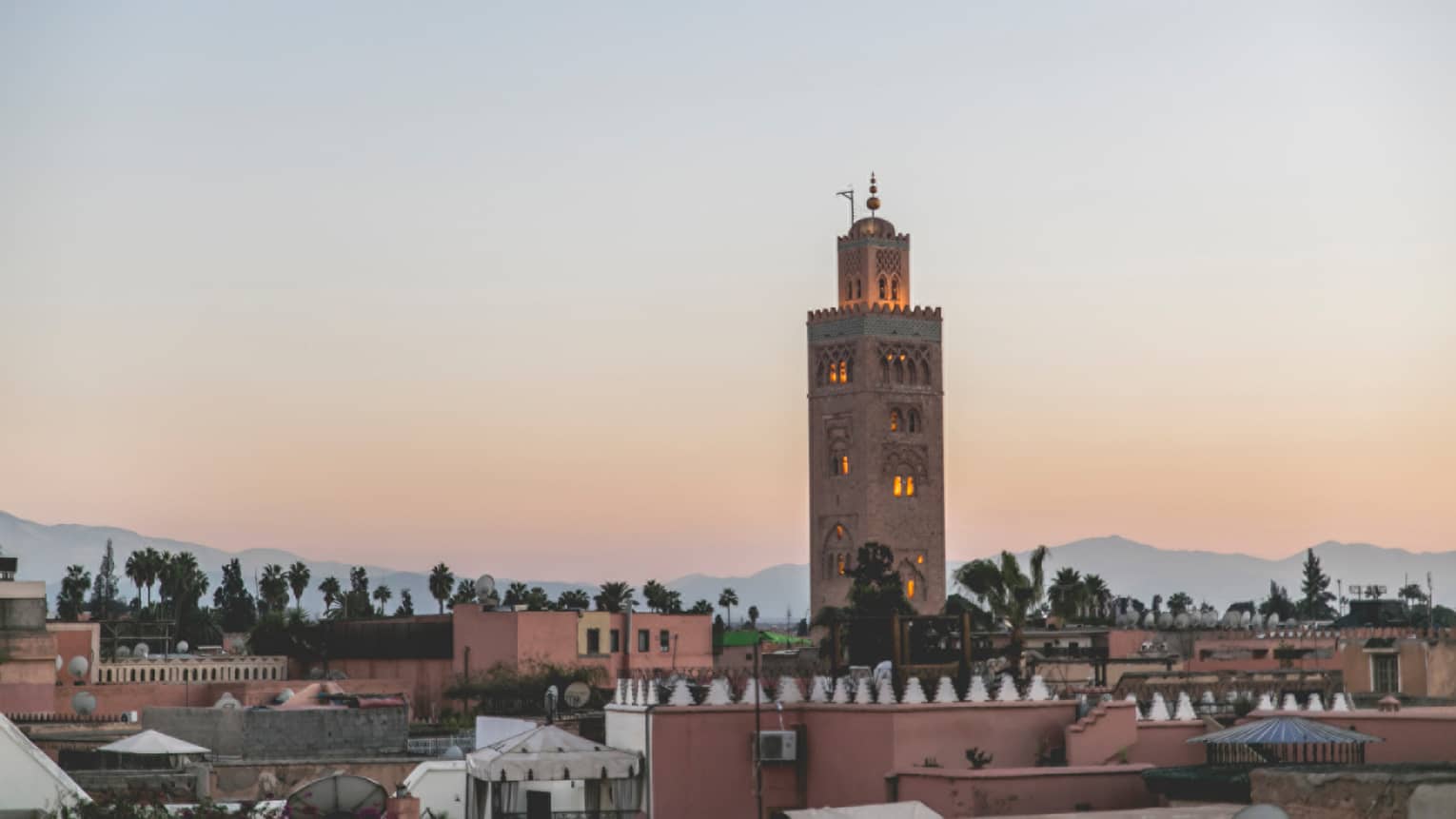 Marrakech city rooftops, tall brick tower against sunset 