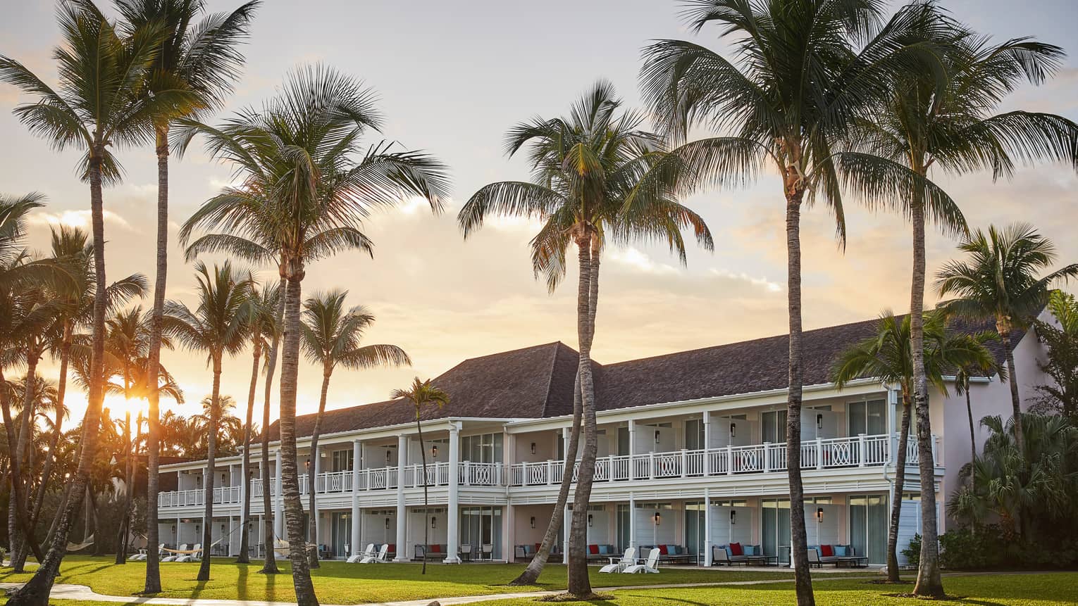 Luxury resort two-story building surrounded by tall palm trees at sunset