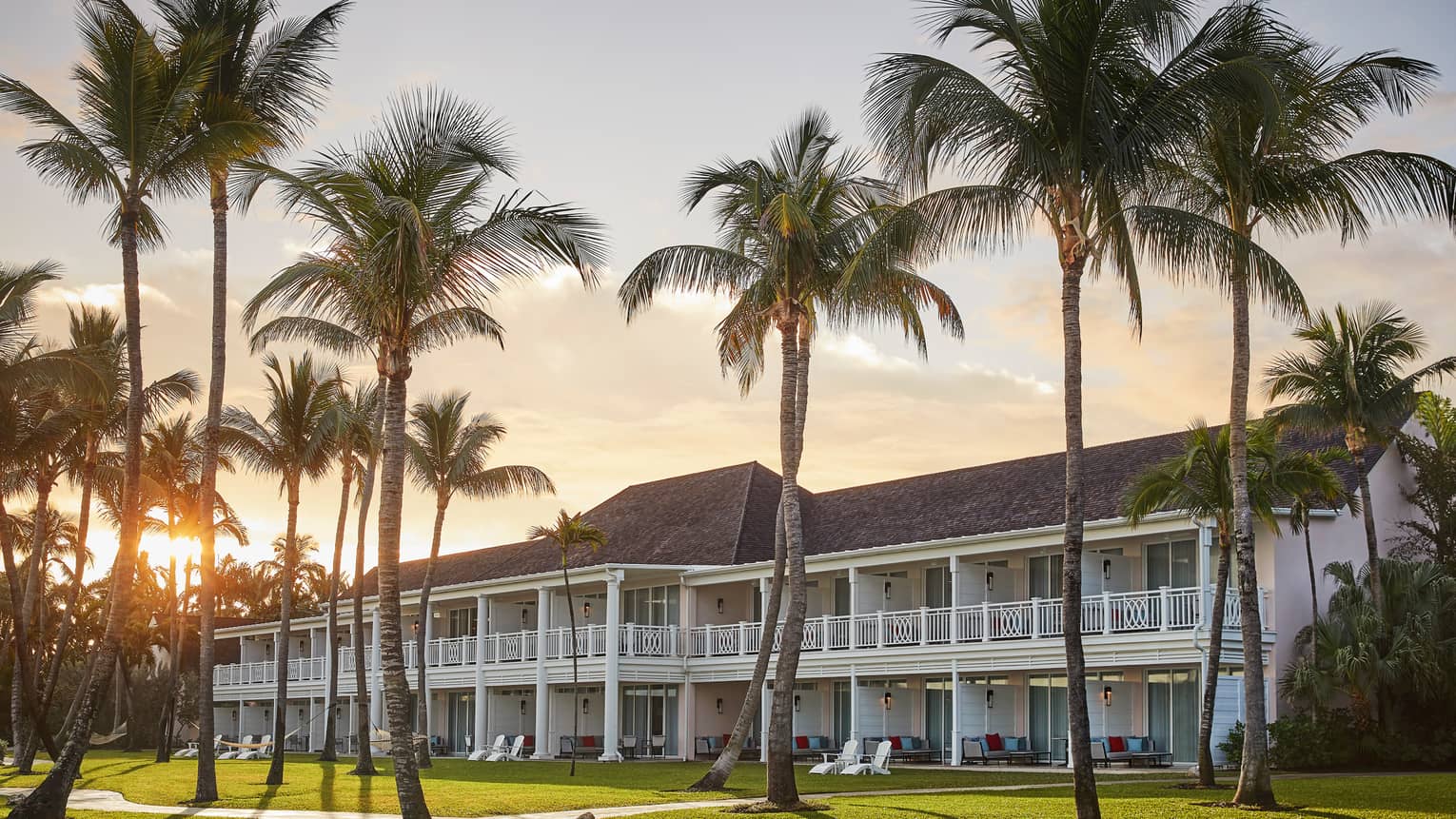 Tall palm trees, sunset over Hartford Wing two-storey white resort building with decorative balconies