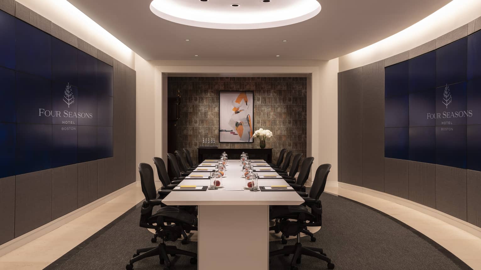 A meeting room with a large white boardroom table surrounded by black chairs with wheels.