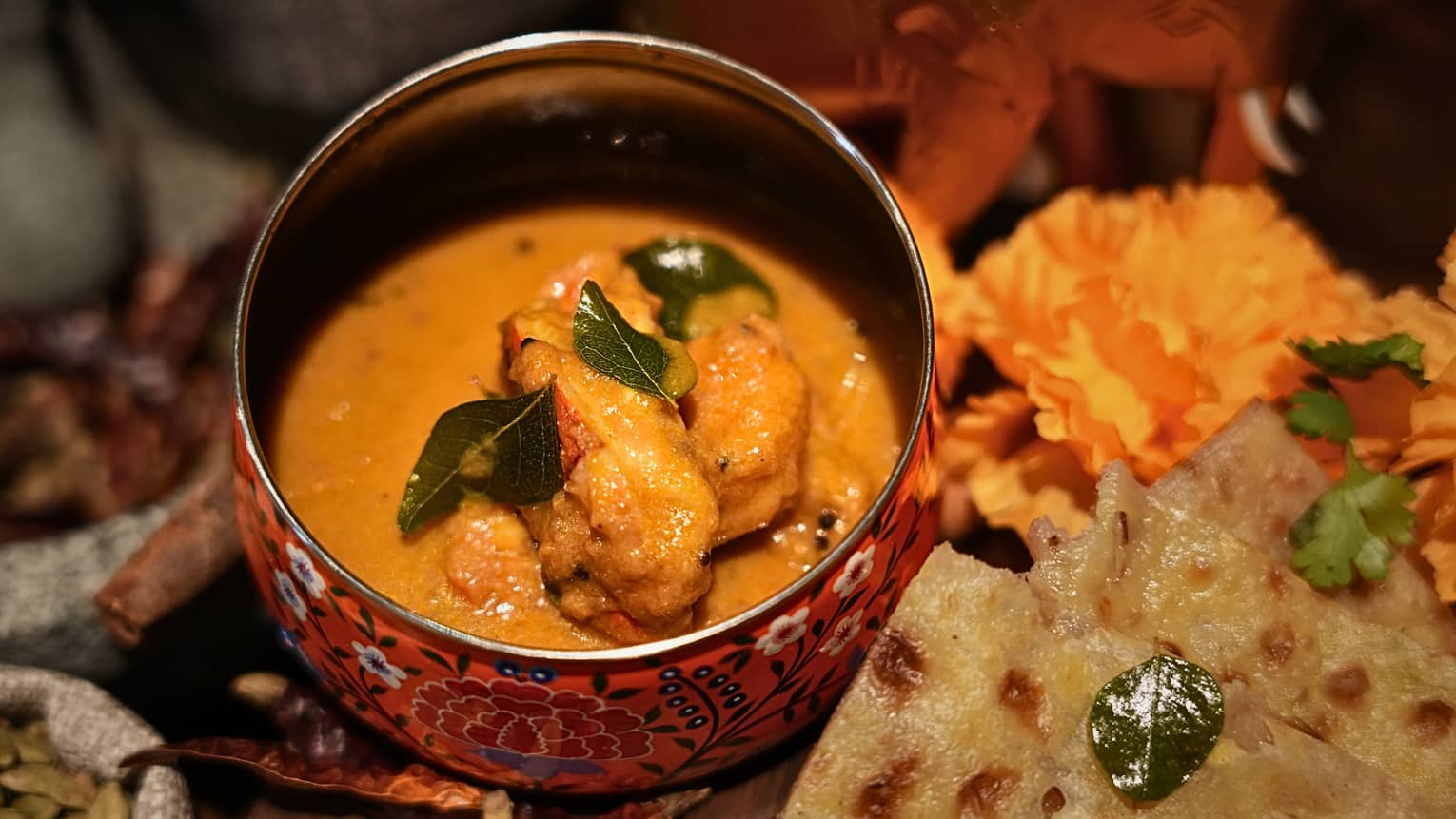 A curry dish in a decorative bowl, surrounded by plates and bowls of other food items