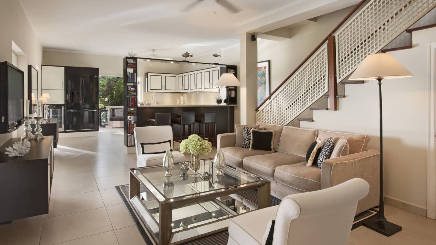 Interior living room of a private villa, featuring a beige sofa, two arm chairs, large square coffee table and ceiling fan