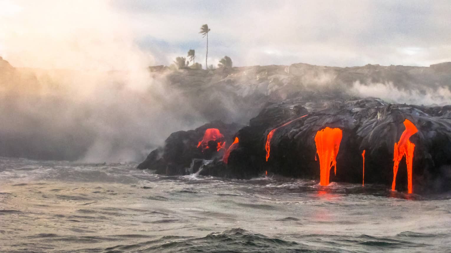 Steam rises from hot lava flowing over black rocks into ocean