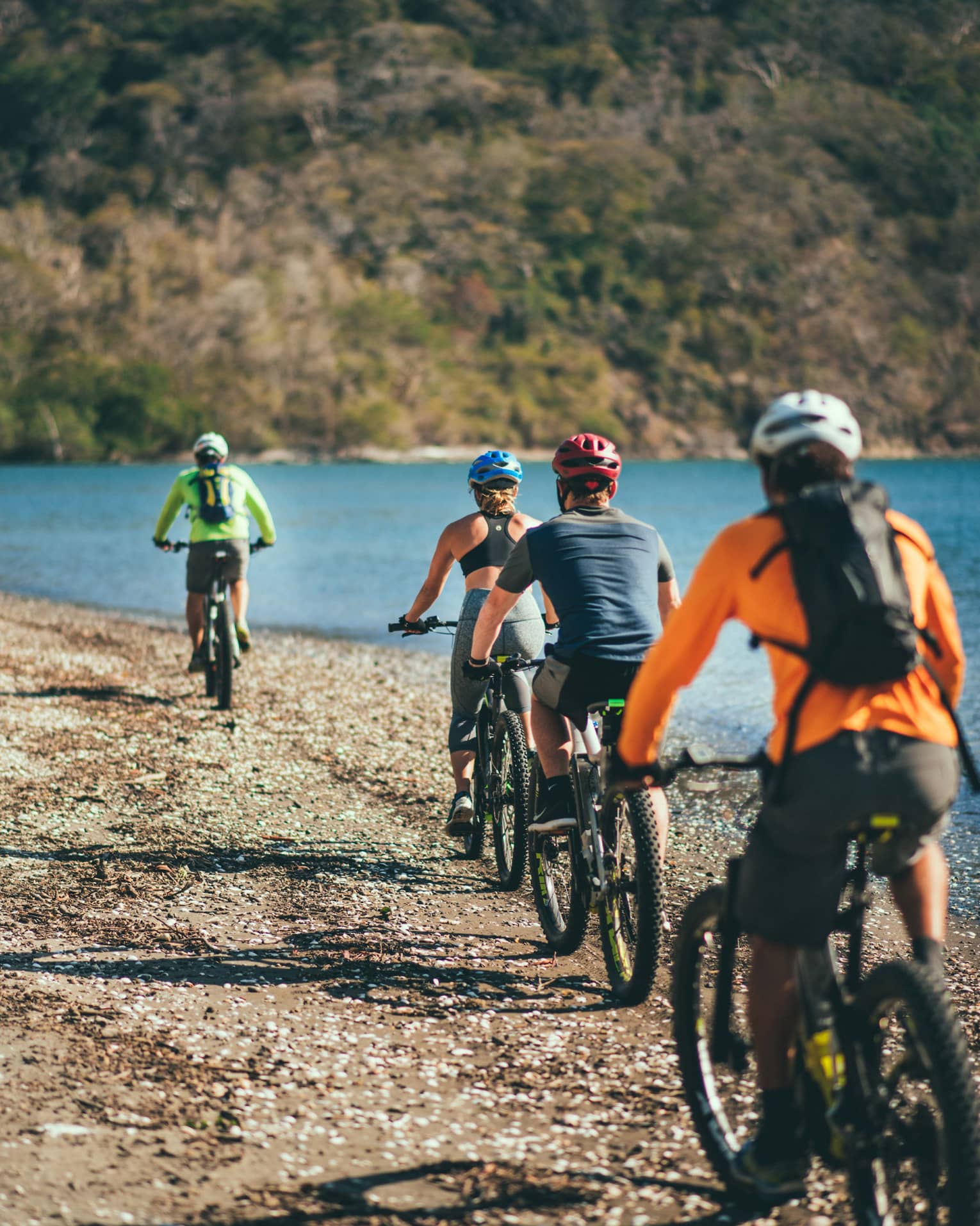 Four people riding bicycles through a rocky terrain next to the ocean