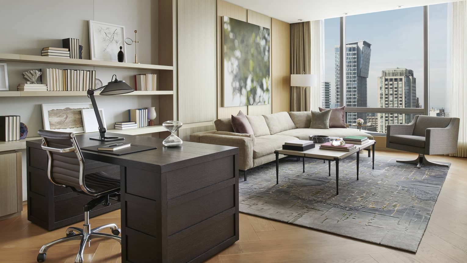 A brown mahogany desk overlooks a seating area with floor-to-ceiling windows.