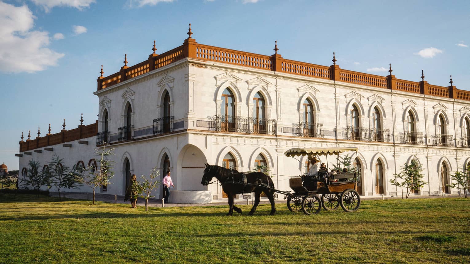 Guests enjoying a horse-drawn carriage ride around a large white building with several beautifully carved arched doorframes.