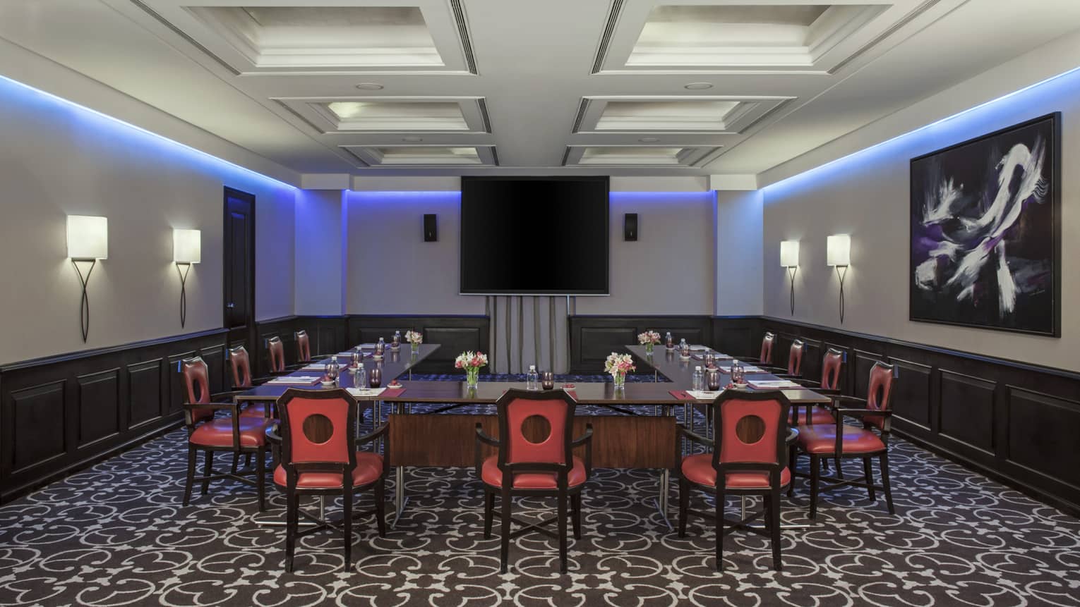 Piero Meeting Room with modular tables and red chairs facing screen, purple accent lighting along ceiling