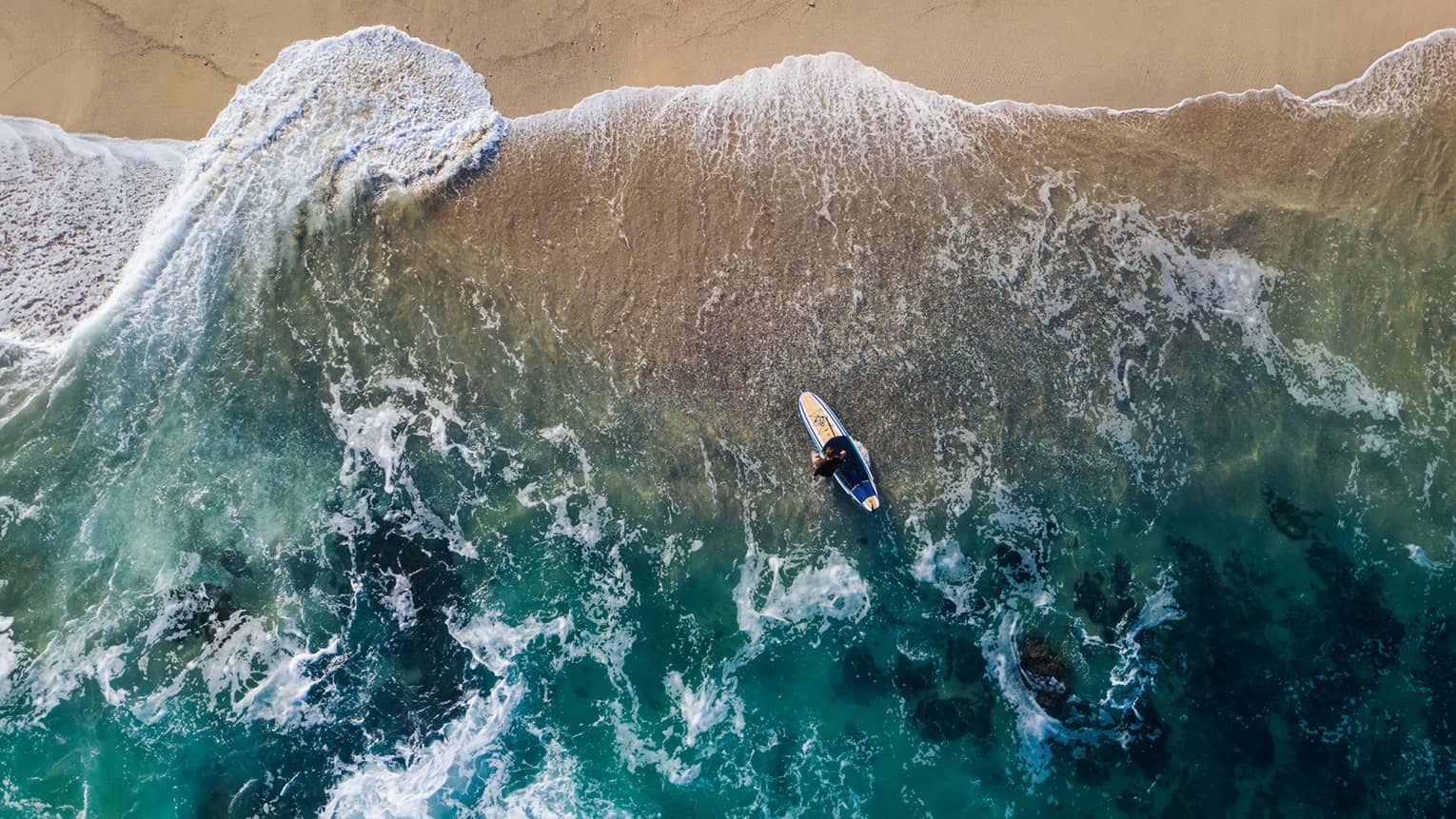 Aerial view of a person paddle boarding in the ocean by the beach