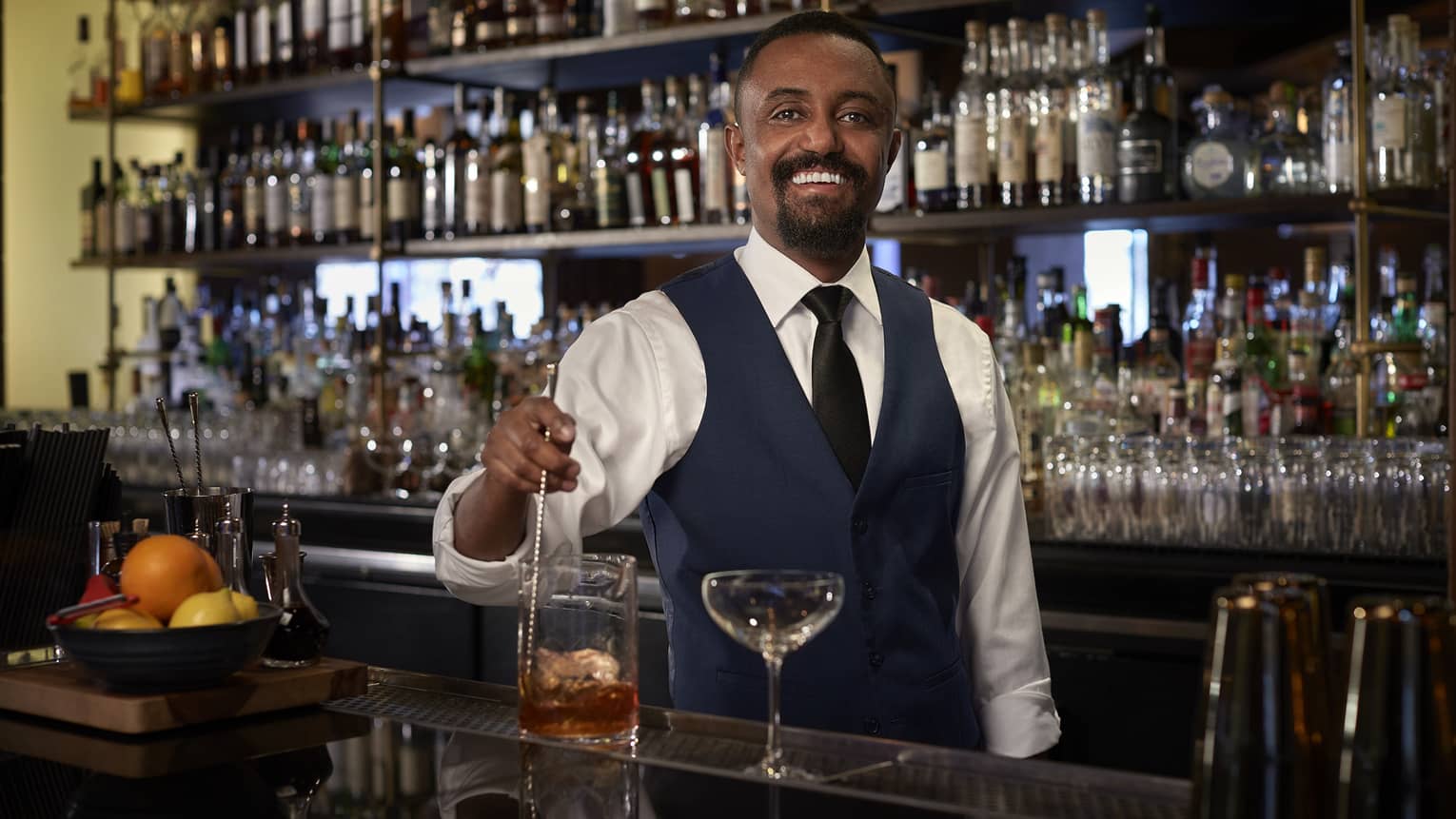 A bartender making a cocktail in front of a wall full of alcohol and drinks.