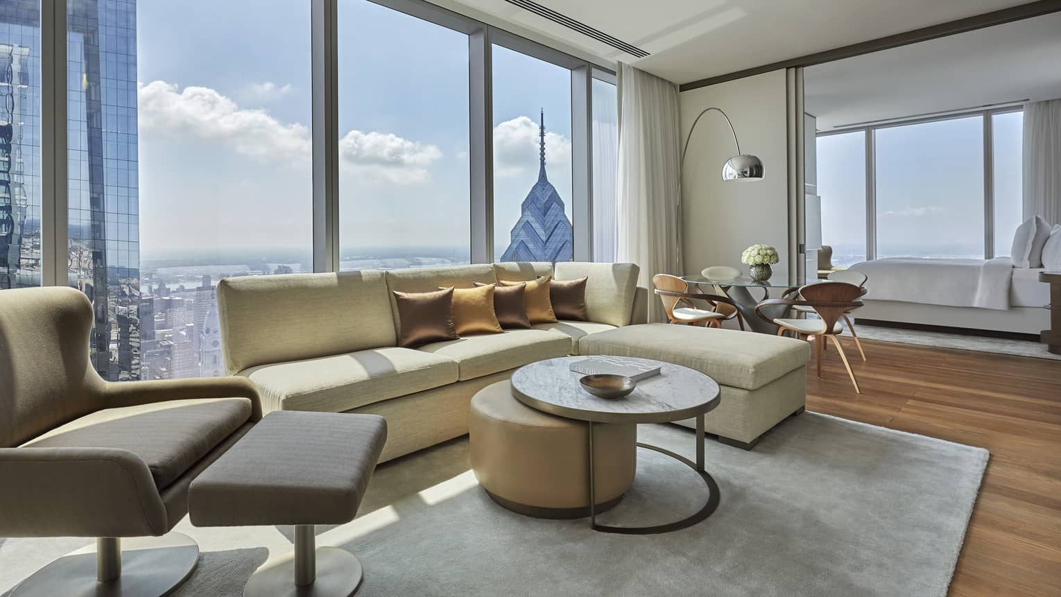 Modern living area with light yellow l-shaped sofa, arm chair, coffee table, Philadelphia city view