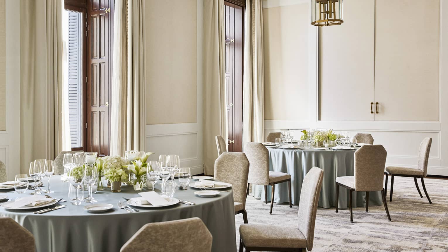 Room with two round banquet tables, each with light green table clothes and six chairs, place settings