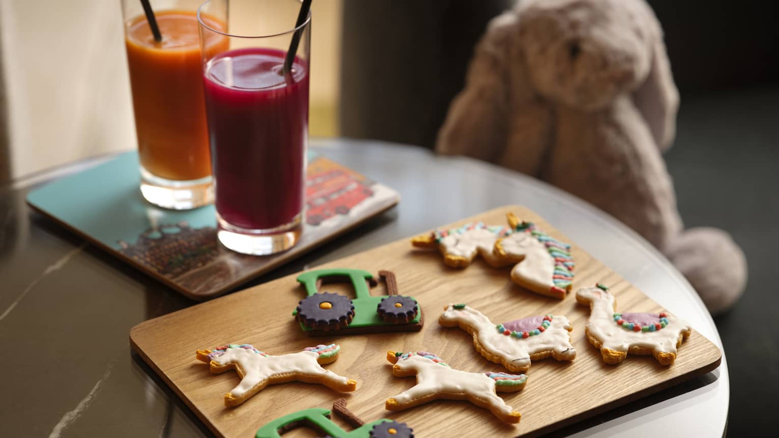 Kids tractor, unicorn and lama cookies on a wooden cutting board next to juice glasses