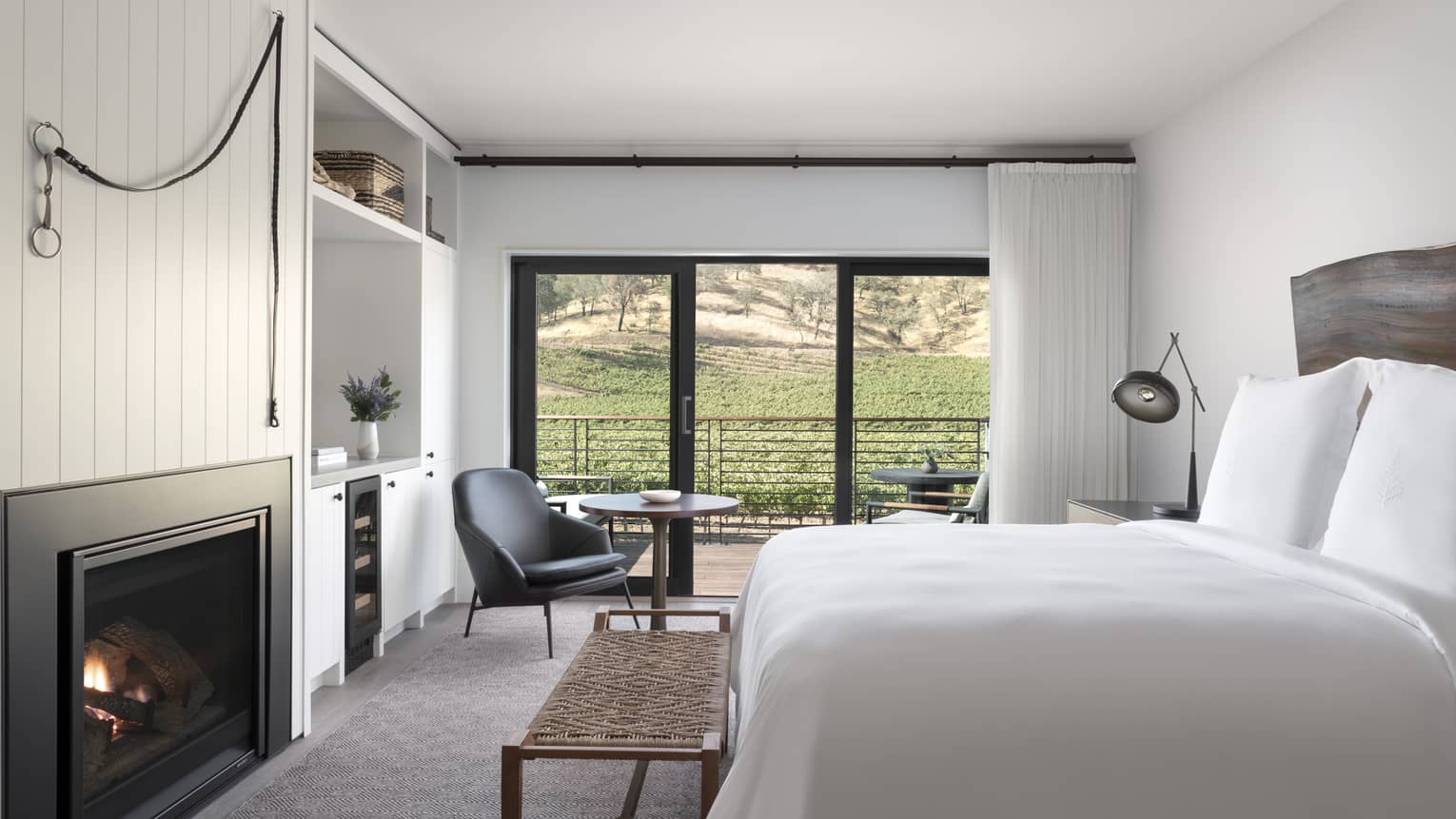 Luxury resort room with a king bed, fireplace, wooden headboard, lounge chair and balcony overlooking vineyard and hillside