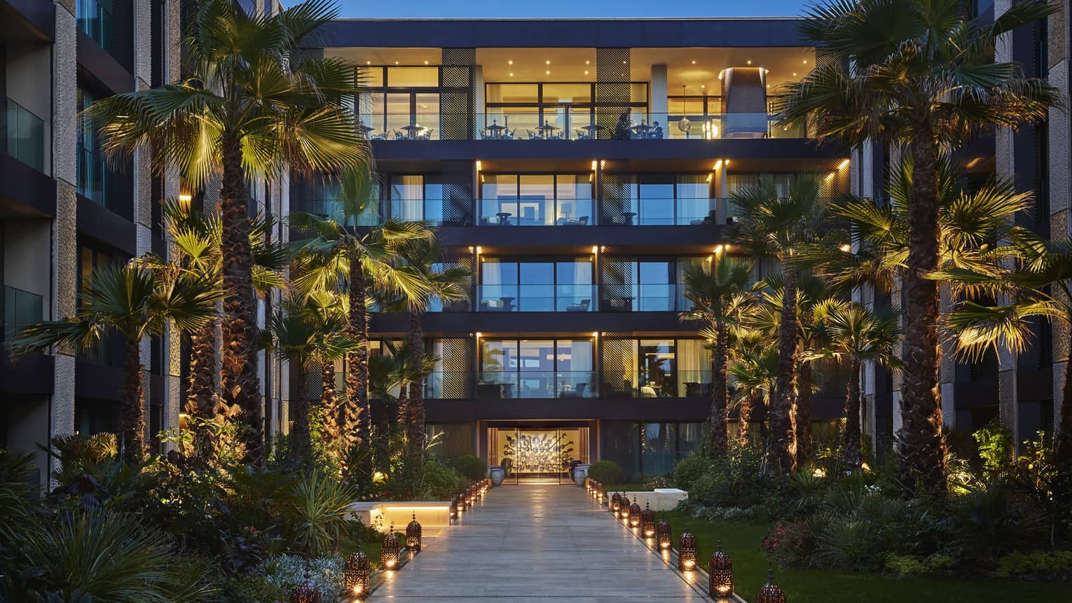 Lanterns. palm trees with lights along walkway under Four Seasons Hotel Casablanca building at dusk