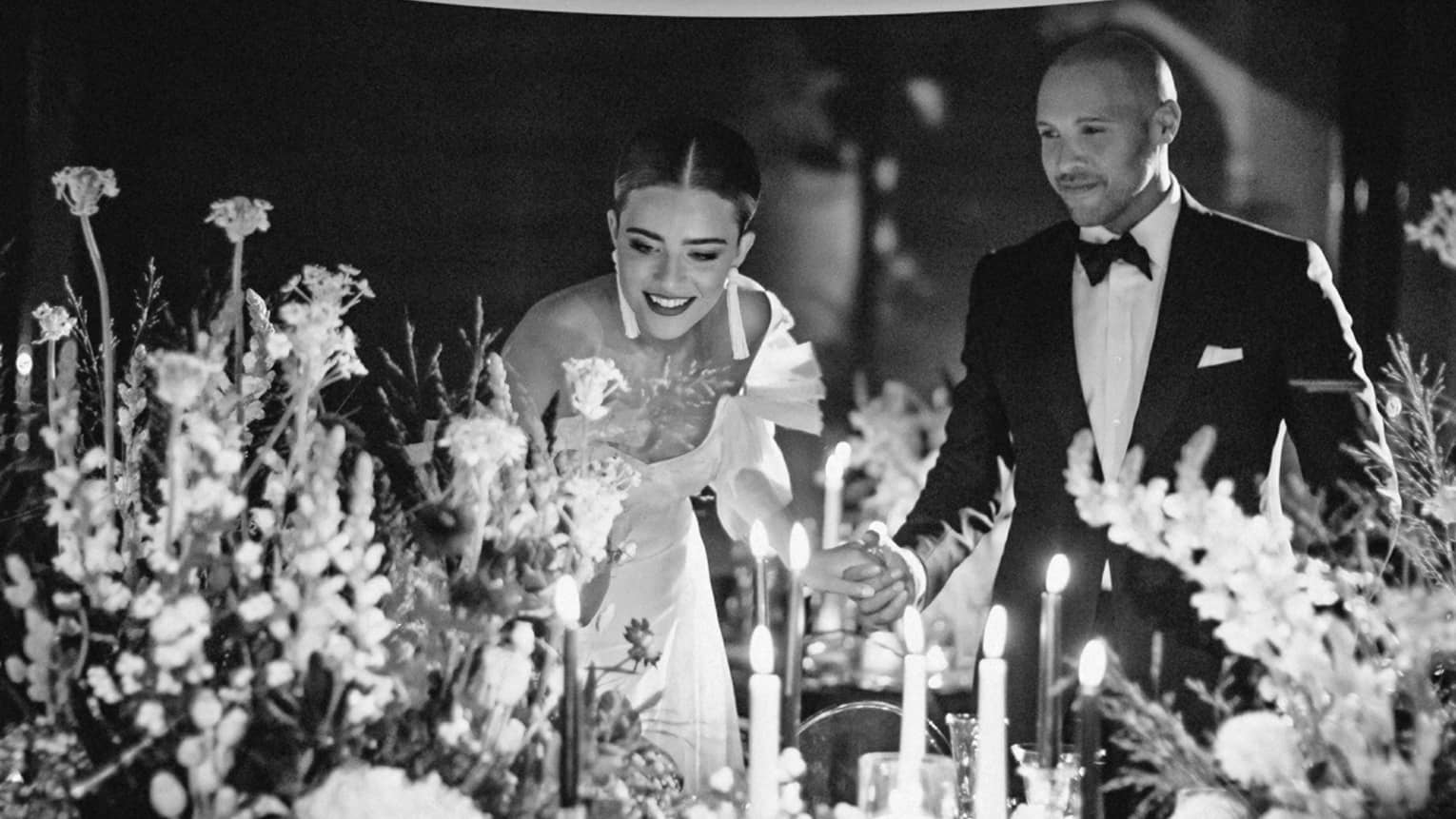 A couple in wedding attire standing behind several large flower arrangements.