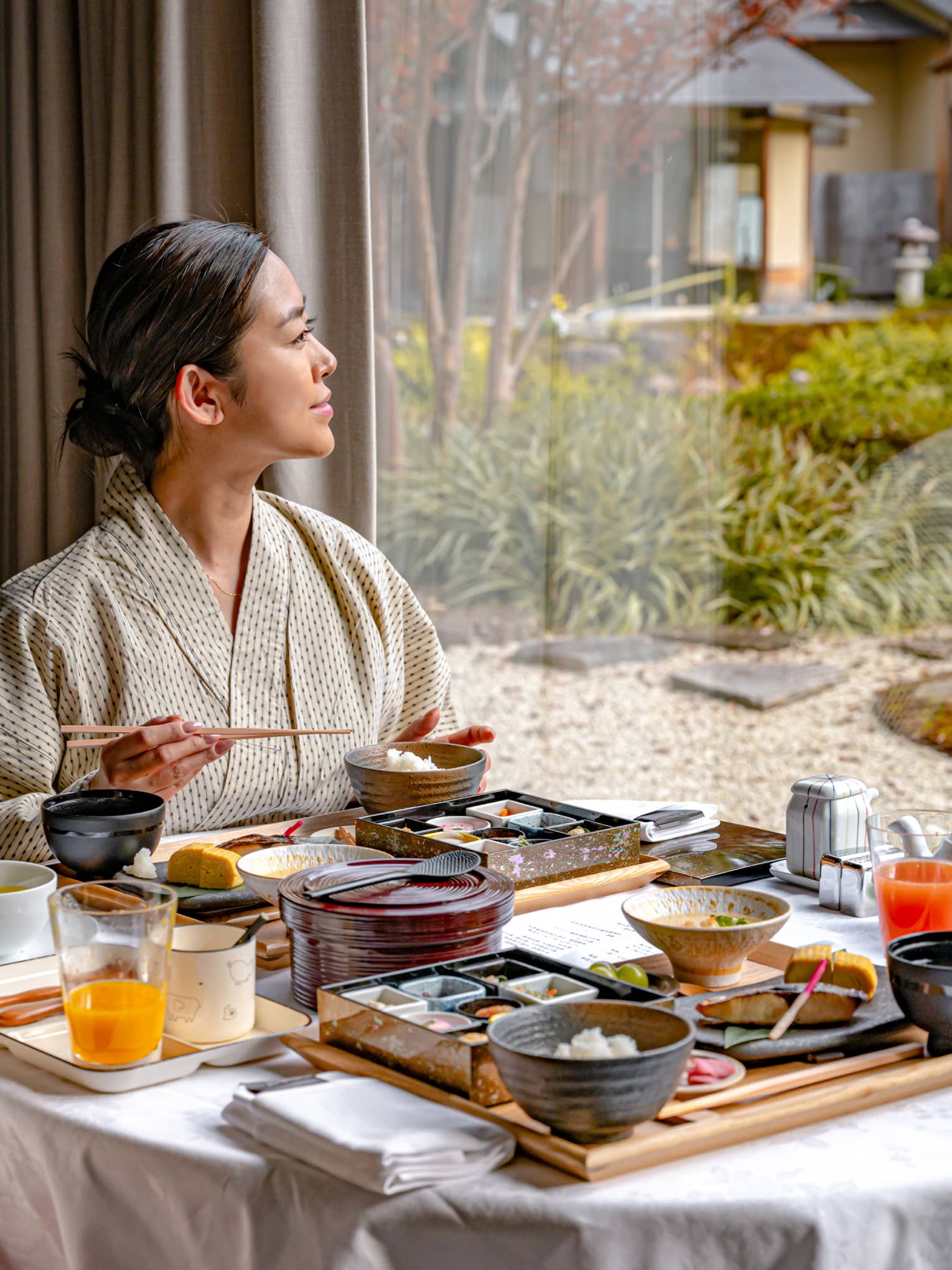 Woman eats breakfast in luxury hotel looking out window to garden