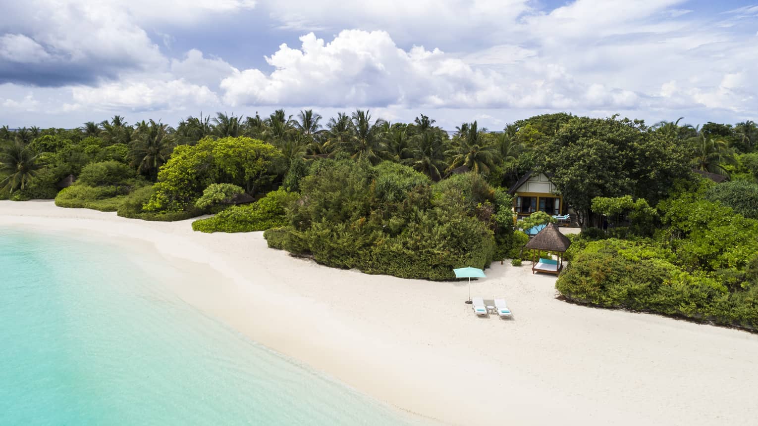 Quiet white-sand beach in the Maldives with turquoise water and lush green trees inland