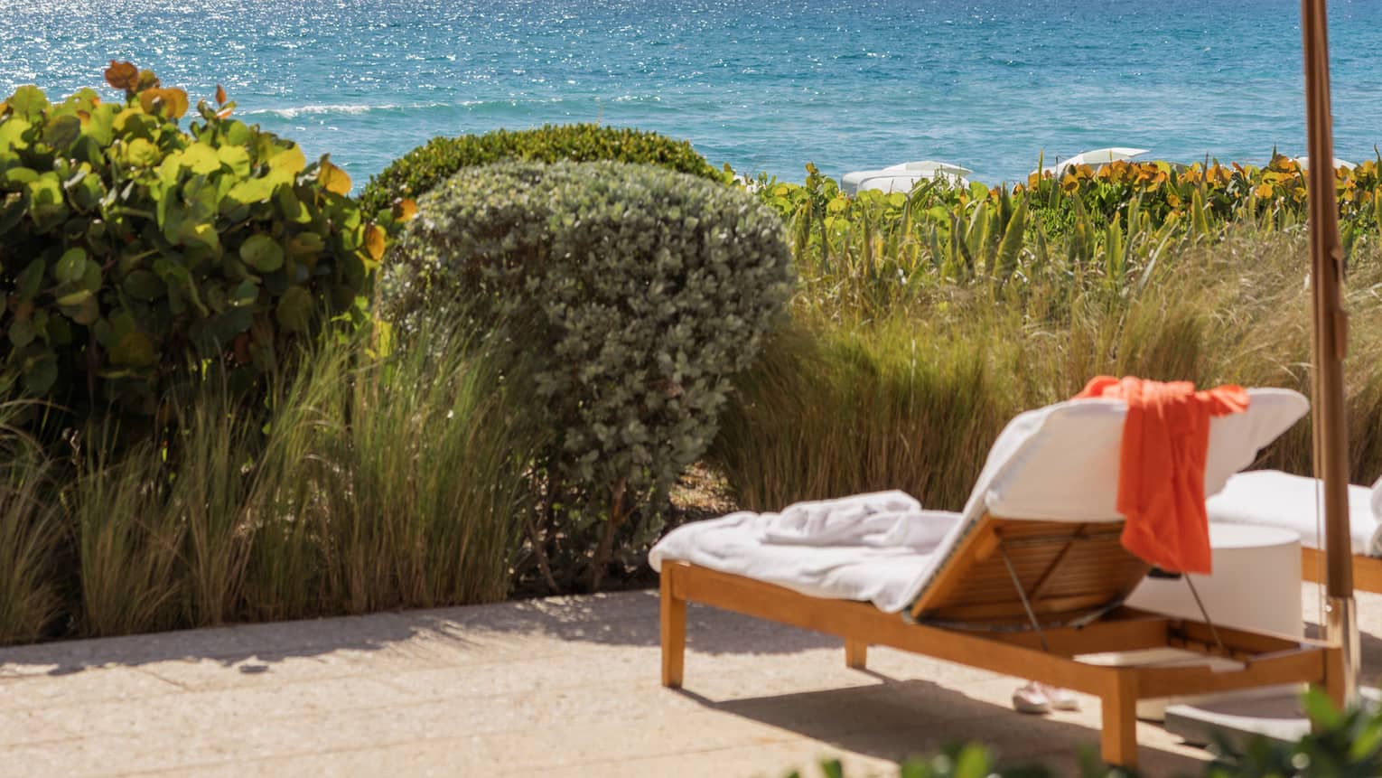 Two lounge chairs set under a pink umbrella sit under a tree with with ocean in the near distance