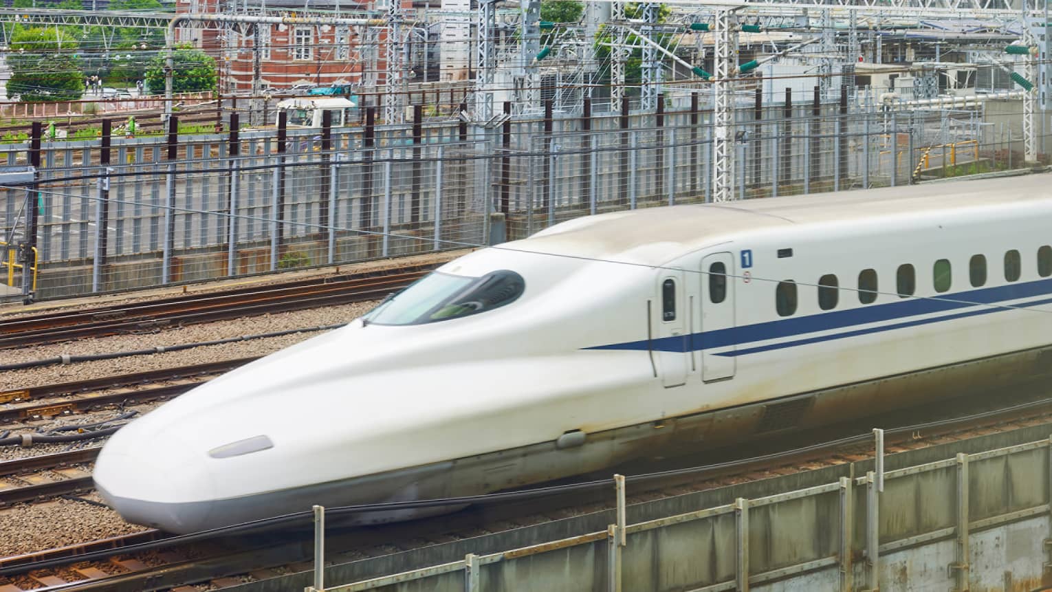 The Shinkansen bullet train speeds past Tokyo's railway station dwarfed by the skyline of rectangular, glass high-rises.