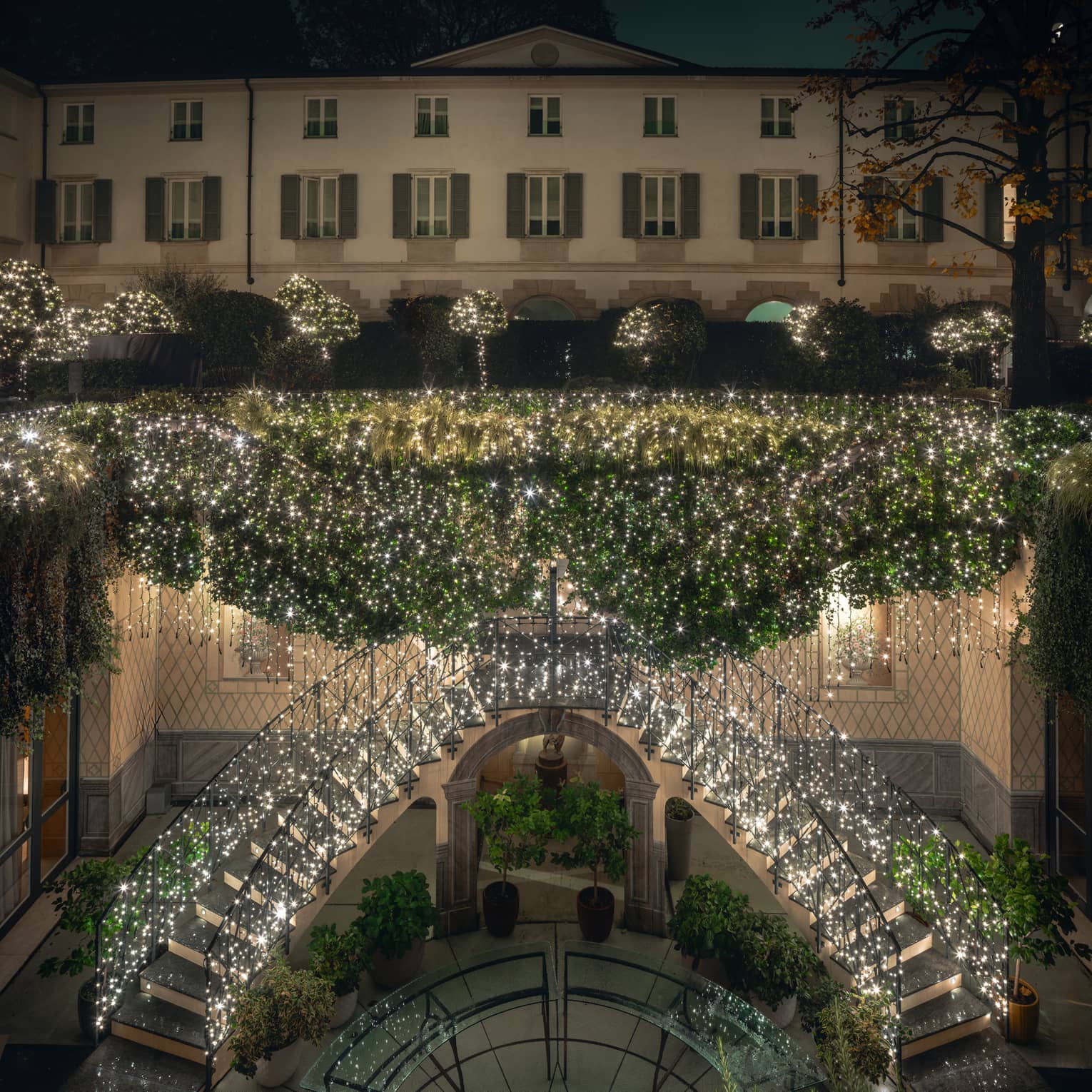 An elegant double staircase in an outdoor space decorated with holiday lights and greenery